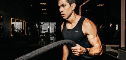 A determined male athlete working out with battle ropes in a dimly lit gym, showcasing strength and fitness.
