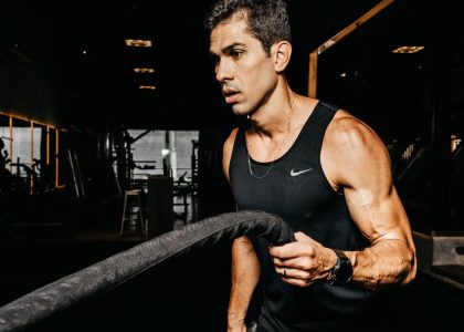 A determined male athlete working out with battle ropes in a dimly lit gym, showcasing strength and fitness.